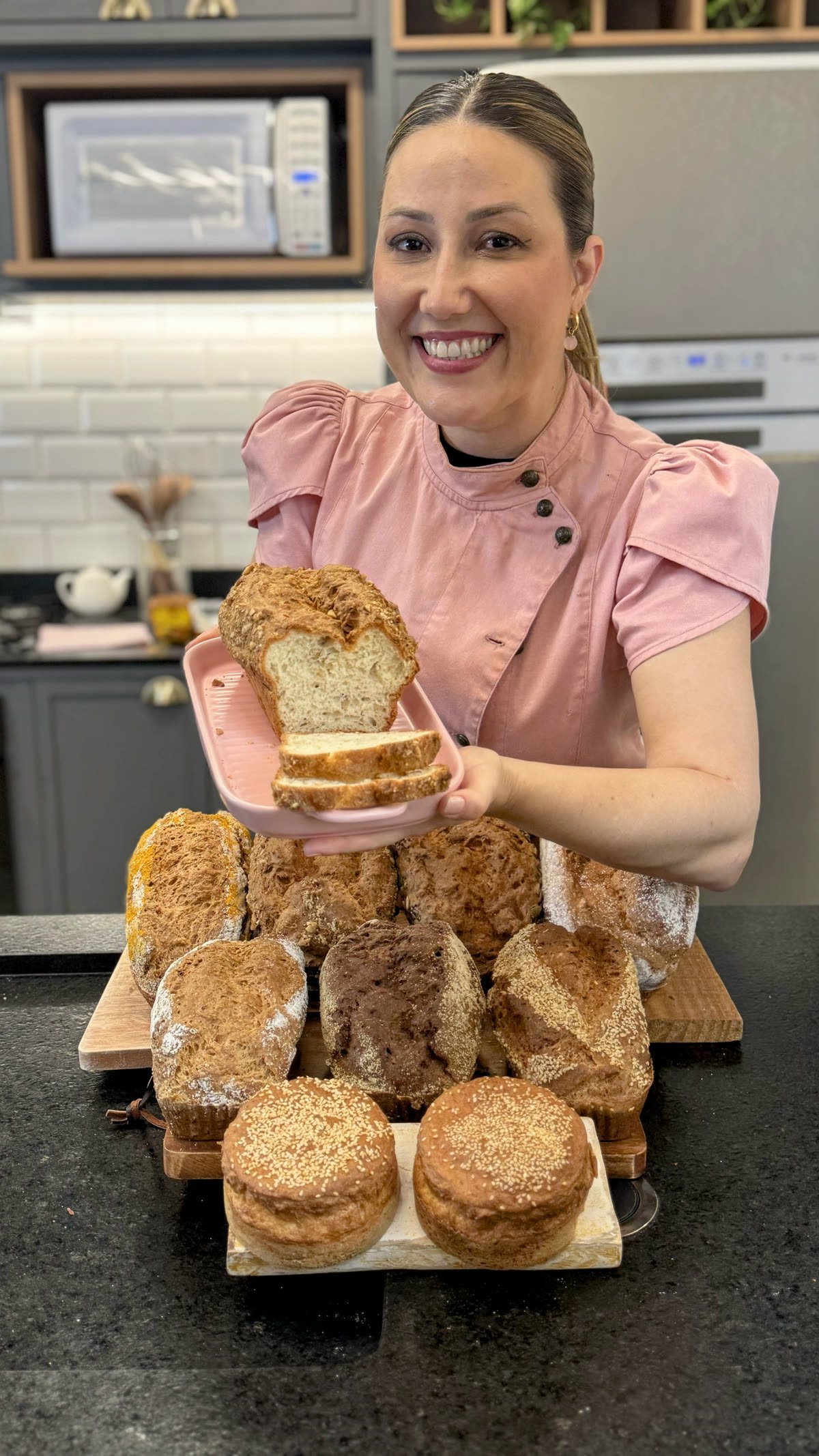 Íris segurando o pão de amêndoas cortado, com vários pães do Método Levíssimo na bancada